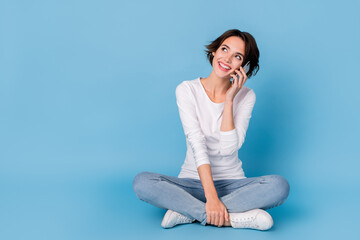 Fototapeta premium Photo of charming dreamy lady dressed white shirt legs crossed talking modern device empty space isolated blue color background