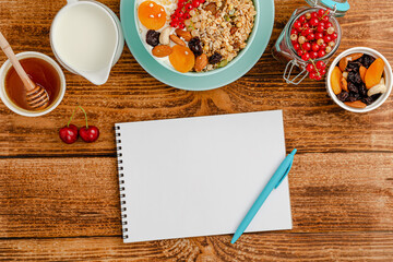 White blank of food diary, healthy breakfast of granola with fruits, milk and honey on wooden table. Top view