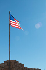 Flag of the United States waving in blue sky with flare