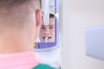 Modern diagnostics in a dental clinic. A man takes a panoramic picture of his teeth. Reflection in the mirror. Rear view.Handsome man. - Powered by Adobe