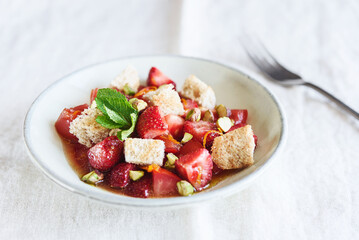Delicious summer salad. Salad bowl with strawberries, tomatoes, pistachios and croutons in honey orange oil sauce on beige linen tablecloth