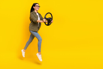 Full length photo of cute young lady jump drive car wear eyewear shirt jeans shoes isolated on yellow background