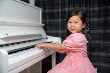Asia girls wearing dress look at camera and smile playing white piano. Enjoying time practicing...