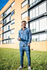 smiling african american young man holding smartphone on sunny day in city or urban area