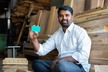 Smiling indian carpenter showing empty green card mockup by looking at camera - concept of employee...