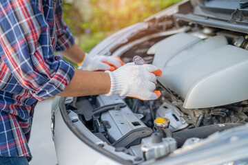 Asian auto mechanic check for repair under the hood of broken down car on the side of the road.