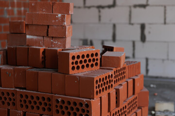 stack of red lightweight clay bricks against a concrete wall. Construction site. Environmentally friendly materials for the construction of load-bearing and dividing walls.