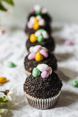 Homemade Easter chocolate cupcakes with chocolate butter cream frosting and candy eggs. Easter brunch. spring blossom decoration. on white linen tableclouth Happy easter day. Easter recipes.