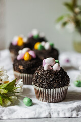 Homemade Easter chocolate cupcakes with chocolate butter cream frosting and candy eggs. Easter brunch. spring blossom decoration. on white linen tableclouth Happy easter day. Easter recipes.