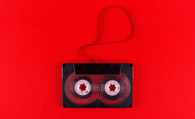 Black audio cassette with pulled out audiotape on red background