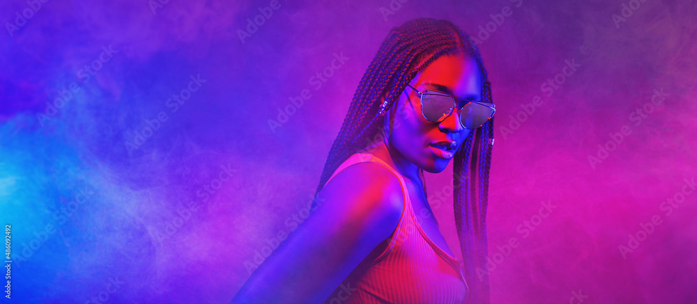 Wall mural portrait of fashion young girl in cool sunglasses in red and blue neon light in the studio