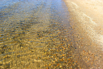Close-up and top view of shiny transparent yellow sand and stones on the beach with clear water. clear sea, the river reveals the beauty of a natural resting place in the summer under the sun. 