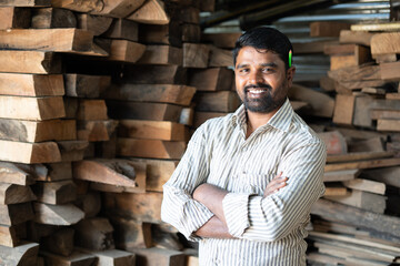 Confident smiling carpenter with arms crossed standing by looking at camera - concept of self...