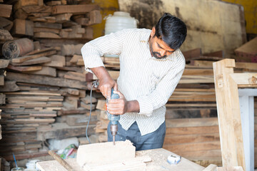 carpenter drilling wood using machine at workshop - concept of craftperson, skilled profession and...
