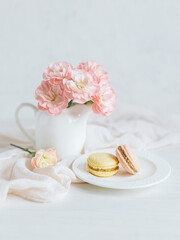 Two tasty French macarons and a jar with pink carnation flowers on a white background.
