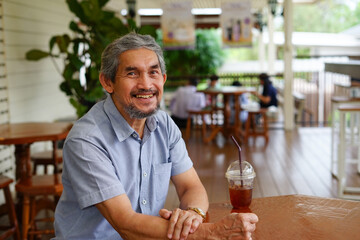 smiling senior man sitting casually in cafe outdoor and a cup of iced coffee on table
