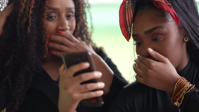 Mother and daughter reacting with shock to content online holding smartphone two people surprise reaction