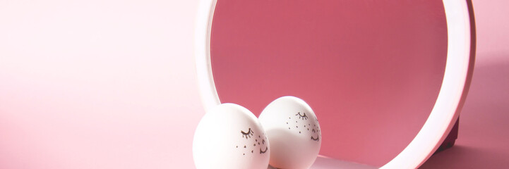 Easter holiday concept with cute handmade egg. Cute face egg looks in the mirror on a pink background. Banner