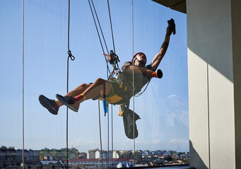 Industrial mountaineering worker hanging on climbing rope and cleaning window of high-rise...