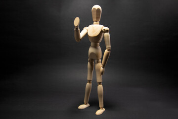 The wooden mannequin raising arm and greets. on a black background