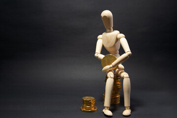 Model of a wooden figure sitting on a pile of coins being happy, holding a coin in his arms on a black background. Business concept