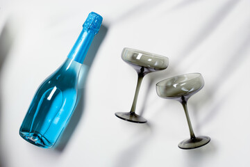 Blue champagne or sparkling wine bottle, champagne glasses from tinted gray glass on white background. Festive drink minimal concept. Modern wine glasses, dark colored glass