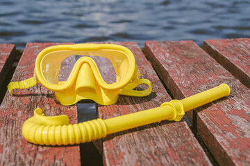 Close-up, yellow waterproof mask for snorkeling, diving with a snorkel on a wooden pier. Seascape...