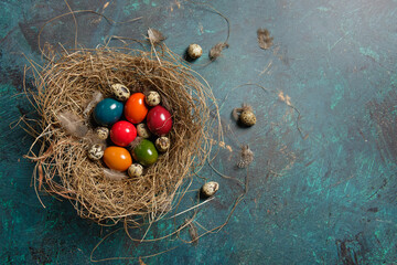 Fototapeta na wymiar Colored Easter eggs and quail eggs in a nest of hay on green background. Flat lay with copy space.