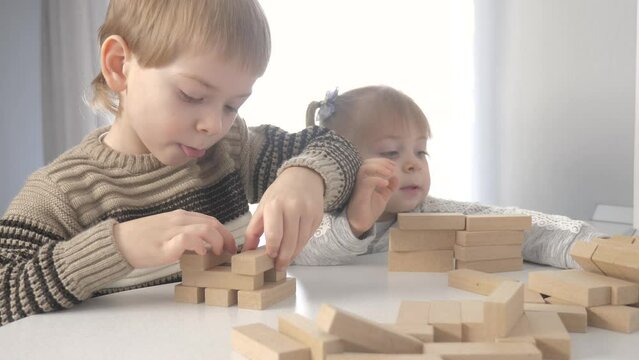 children play in designer wooden sticks teamwork. happy family kids little boy and girl play in wooden blocks cubes build a house. brother and sister collect designer development of fine lifestyle