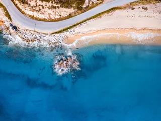 Muurstickers Luchtfoto strand Luchtfoto van een idyllisch zee zandstrand met kronkelende asfaltweg en rotsachtige klif. Achtergrond voor reizen en vakantie