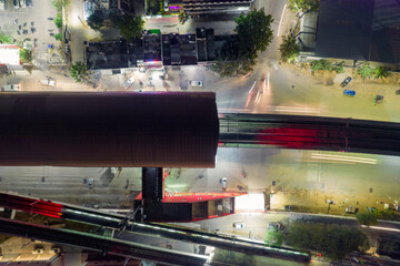 top down flat aerial shot showing red roof of elevated metro train station with track coming out over busy street with cars in bangalore gurgaon india