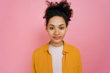 Obraz na płótnie Canvas Portrait of positive beautiful millennial african american girl with curly hair and freckles, wearing casual stylish clothes, standing over isolated pink background, looking straight at camera