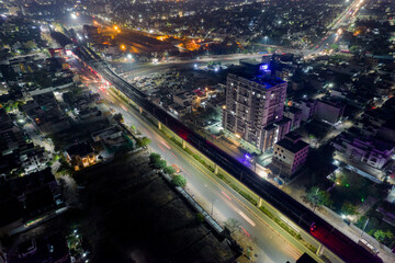 aerial drone shot with elevated metro train tracks over busy street with light trails from traffic skyscrapers on side in hyerabad jaipur india