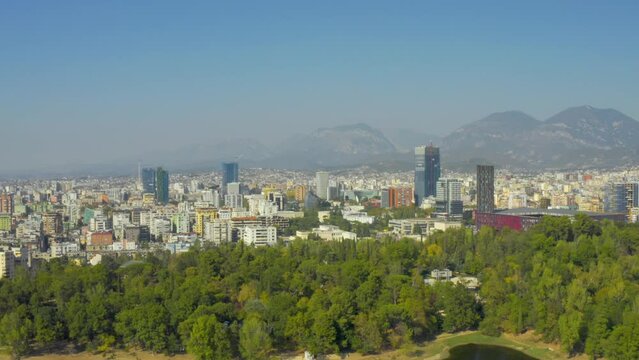 A drone view of the skyline of Tirana, Albania. Park on the Artificial Lake, Grand Park of Tirana, mountains, skyscrapers, city, aerial, downtown, park - 4K Drone Video Footage