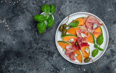 Antipasti. Fresh melon with prosciutto and basil on dark stone table. Italian food. Long banner...