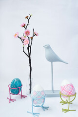 Easter card, Multi-colored Easter eggs on legs, a figurine of a bird and a branch of sakura on a white background