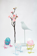 Moscow, Russia, February 2022, spring Easter still life, a figurine of a bird, a sakura branch in a jar and three Easter eggs with bird legs on a white background