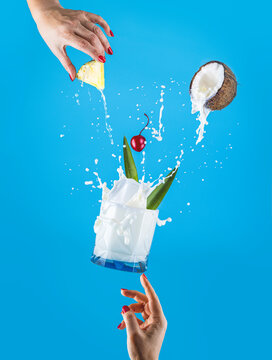 Woman hands support fly glass of tasty Frozen Pina Colada Traditional Caribbean cocktail with splash,  ingredients falling in glass