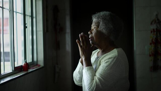 Spiritual older woman in 80s praying at home by window