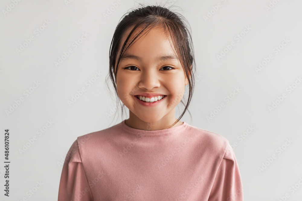 Wall mural Headshot Of Toothy Chinese Kid Girl Posing Smiling, Gray Background