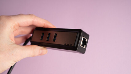 Black USB hub in hand. Three ports USB charger isolated on violet