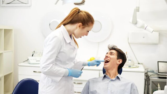 Young friendly female dentist talking with male patient sitting in chair about oral health hygiene