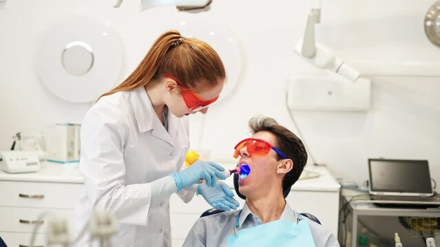 Friendly female dentist talking with smiling male patient speaking after composite dental filling