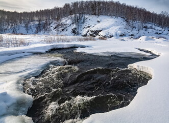 Winter landscape with birch trees on the mountain shore, snow and flowing river water