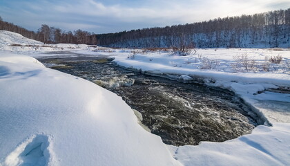 Winter landscape with birch trees on the mountain shore, snow and flowing river water