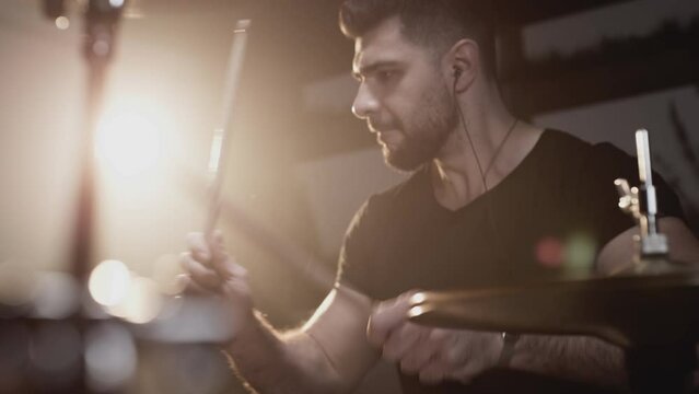A handsome guy plays drums in a recording studio. Making music by an indie artist. Rock style in the school of creativity. Learns to play the drum kit, beats the rhythm. Rocker plays solo. Slow motion