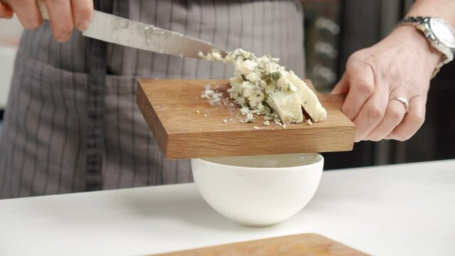 Crop chef adding blue cheese into bowl from board