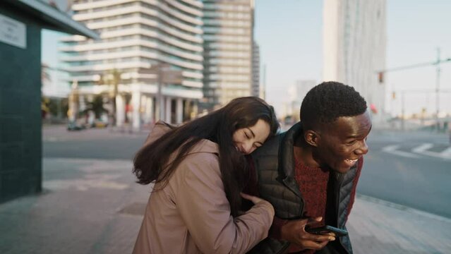 Cheerful multiethnic couple laughing at joke in city