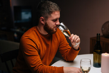 Close-up of happy bearded young man drinking champagne from glass sitting together with wife at dinner table with candles in dark room. Love man and woman celebrating anniversary, Valentines day.