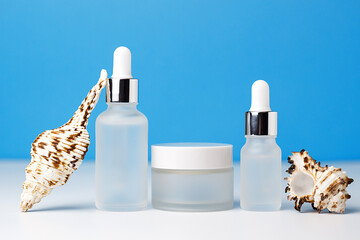 White frosted glass jar of seashell cream on a blue and white background. Cosmetics and cosmetology. Mockup for products. Nautical and summer concept. SPF protection from sun and wind.